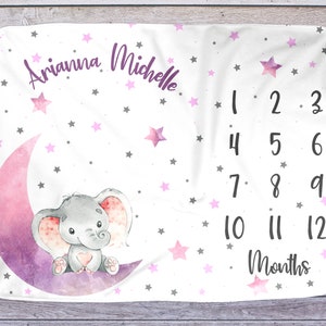 Puede incluir: Una manta de beb&eacute; blanca con una luna de acuarela rosa y morada y un elefante gris sentado sobre ella. La manta est&aacute; decorada con estrellas rosas y grises y tiene el texto "Arianina Michelle" y "1 2 3 4 5 6 7 8 9 10 11 12 Meses" impreso en ella.