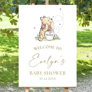 May include: White welcome sign with a Winnie the Pooh illustration. The sign says "Welcome to Evelyn's Baby Shower 10.14.20XX".