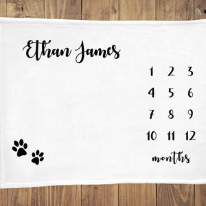 May include: White baby milestone blanket with black paw prints and the text "Ethan James" and numbers 1-12 with the word "months" below.
