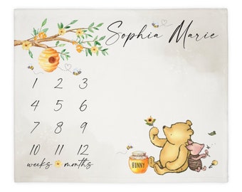 May include: A Winnie the Pooh and Piglet baby milestone blanket with a beehive and flowers. The blanket has a white background with black numbers 1-12 and the words "weeks" and "months". The blanket is personalized with the name "Sophia Marie".