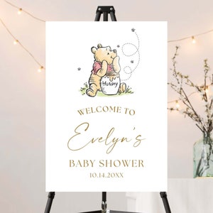 May include: A white welcome sign with a Winnie the Pooh illustration. The sign says "Welcome to Evelyn's Baby Shower 10.14.20XX".