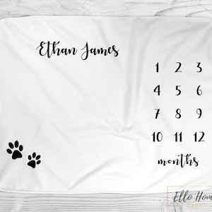 May include: White baby blanket with black paw prints and the text "Ethan James" and a number chart for tracking a baby's growth from 1 to 12 months.