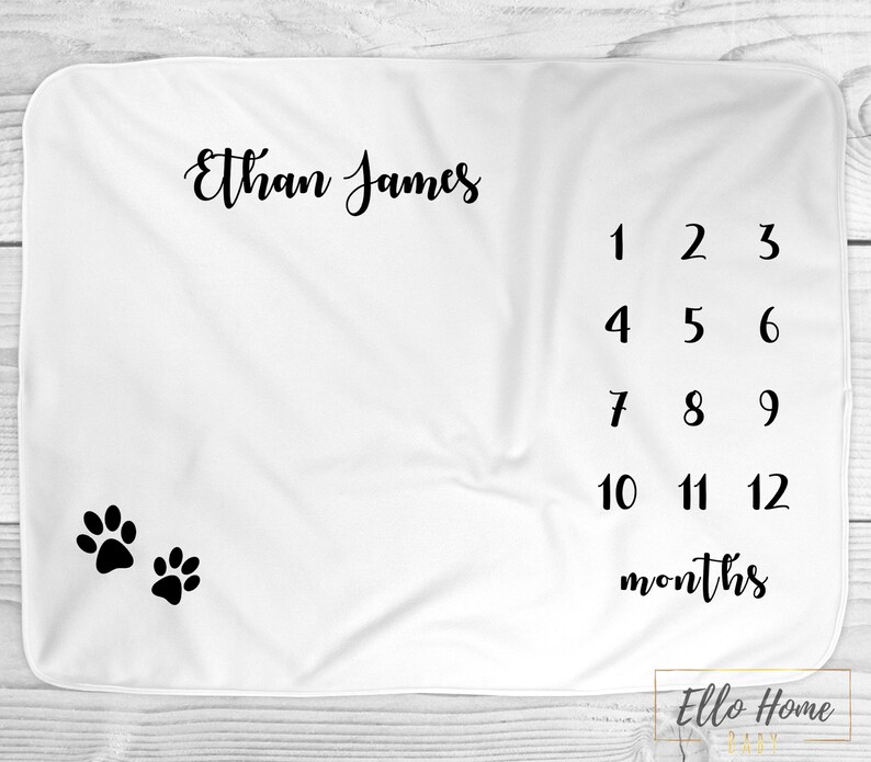 May include: White baby blanket with black paw prints and the text "Ethan James" and a number chart for tracking a baby's growth from 1 to 12 months.