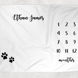May include: White baby blanket with black paw prints and the text "Ethan James" and numbers 1 through 12 with the word "months" below.