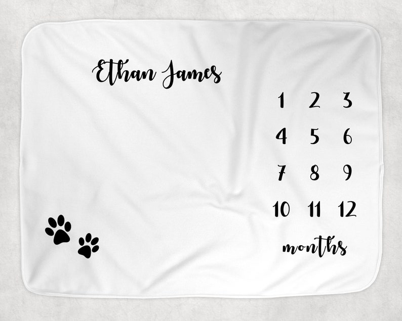 May include: White baby blanket with black paw prints and the text "Ethan James" and numbers 1 through 12 with the word "months" below.