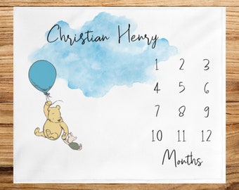 Könnte beinhalten: Eine Winnie Puuh Baby-Meilenstein-Decke mit einer blauen Aquarellwolke und einem blauen Ballon. Die Decke hat eine Tabelle mit den Zahlen 1 bis 12, um das monatliche Wachstum eines Babys zu verfolgen. Der Text "Christian Henry" befindet sich oben auf der Decke.