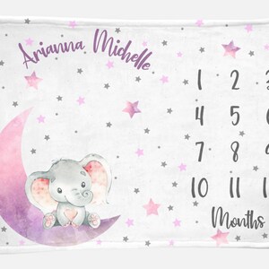 Puede incluir: Una manta blanca para hitos de beb&eacute; con una luna creciente rosa y morada y un elefante gris sentado sobre ella. La manta est&aacute; decorada con estrellas rosas y grises. El texto "Arianna Michelle" est&aacute; escrito en la parte superior de la manta. Los n&uacute;meros del 1 al 12 est&aacute;n impresos en el lado derecho de la manta, con la palabra "Meses" debajo.