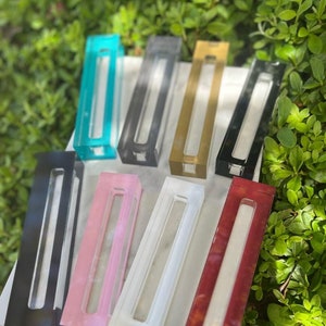 May include: Assortment of eight rectangular acrylic display stands in various colors, including turquoise, gray, gold, black, pink, white, and red. The stands are arranged in a row on a white surface.