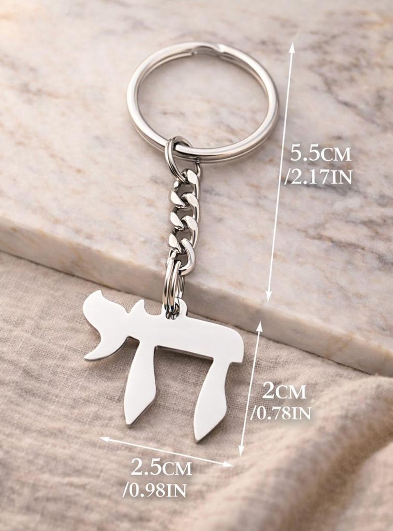 Może przedstawiać: Srebrzysty metalowy brelok do kluczy z hebrajską literą Chai. Całkowita długość wynosi 5,5 cm. Zawieszka ma 2 cm wysokości i 2,5 cm szerokości i jest przymocowana do standardowego okrągłego k&oacute;łka. Wymiary są wyraźnie zaznaczone na zdjęciu.