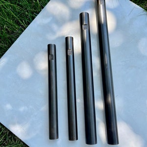 Pode incluir: Quatro tubos de metal preto de comprimentos diferentes, cada um com um pequeno desenho gravado na parte superior.