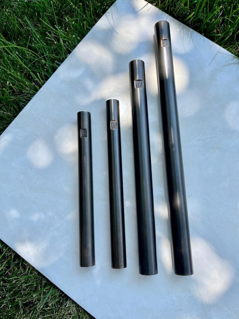 Pode incluir: Quatro tubos de metal preto de comprimentos diferentes, cada um com um pequeno desenho gravado na parte superior.