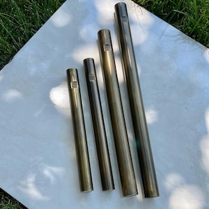 Pode incluir: Quatro tubos met&aacute;licos de comprimentos diferentes, cada um com um n&uacute;mero gravado na parte superior. Os tubos s&atilde;o de cor dourado escuro e t&ecirc;m um acabamento liso e polido.