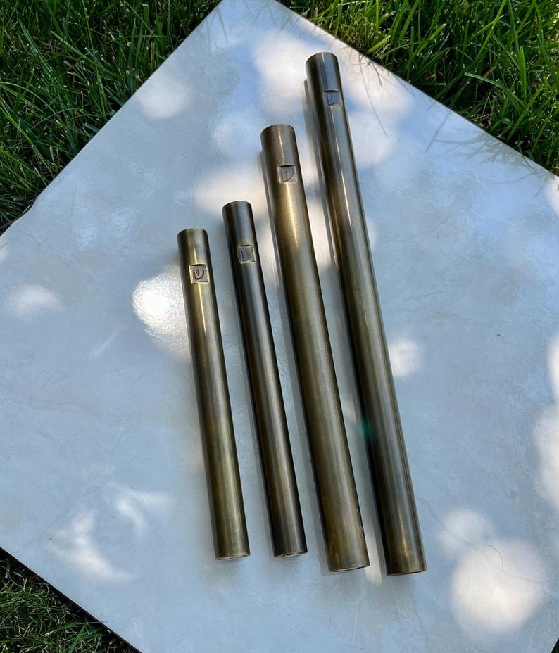 Pode incluir: Quatro tubos met&aacute;licos de comprimentos diferentes, cada um com um n&uacute;mero gravado na parte superior. Os tubos s&atilde;o de cor dourado escuro e t&ecirc;m um acabamento liso e polido.