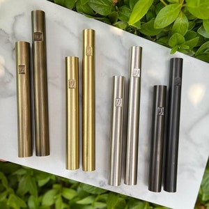 Pode incluir: Sete tubos met&aacute;licos em diferentes acabamentos, incluindo lat&atilde;o, ouro, prata e preto. Cada tubo tem um pequeno desenho gravado no lado.