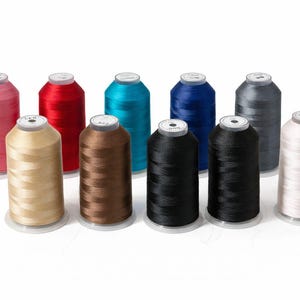 May include: A collection of ten cylindrical spools of embroidery thread arranged in two rows. The colors include pink, red, bright blue, dark blue, grey, beige, brown, black, dark charcoal, and off-white, each with a white circular top label.