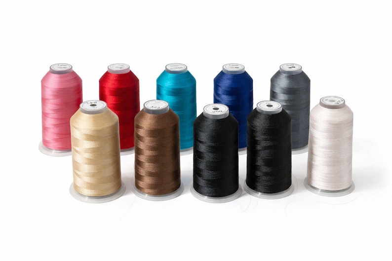 May include: A collection of ten cylindrical spools of embroidery thread arranged in two rows. The colors include pink, red, bright blue, dark blue, grey, beige, brown, black, dark charcoal, and off-white, each with a white circular top label.