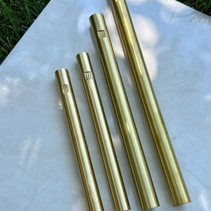 Pode incluir: Quatro tubos de metal de cor dourada de comprimentos diferentes. Cada tubo tem uma pequena letra 'D' gravada na parte superior.