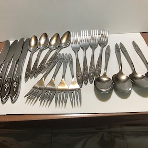May include: A set of silverware with a floral design. The set includes knives, forks, and spoons.