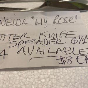 May include: A handwritten note advertising Oneida "My Rose" butter knife spreaders. The note states that there are 4 available for $8 each.