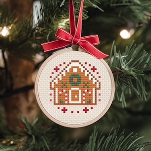 Könnte beinhalten: Ein gestickter Weihnachtsbaumschmuck in Form eines Lebkuchenhauses mit roten und weißen Akzenten.