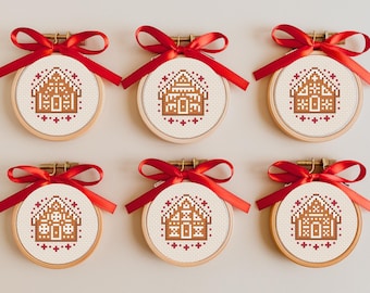 May include: Six small, round, wooden embroidery hoops with red ribbon bows. Each hoop features a cross-stitch design of a gingerbread house.
