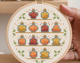 May include: A cross-stitch embroidery hoop featuring a design of 12 colourful potion bottles on shelves. The bottles are in shades of orange, yellow, and red, and have a whimsical, magical feel.