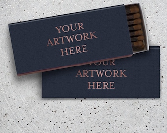 May include: A navy blue matchbox with the text "YOUR ARTWORK HERE" in a rose gold color, placed on a speckled gray concrete tray. The matchbox is open, revealing the match heads. The second matchbox is below it.