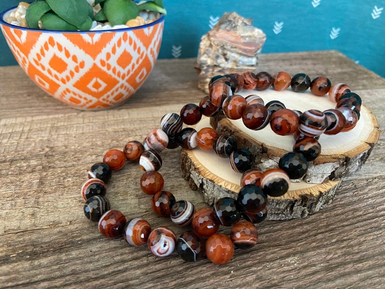 Beads are round and faceted. Three natural red and black banded agate beaded stretch bracelets
