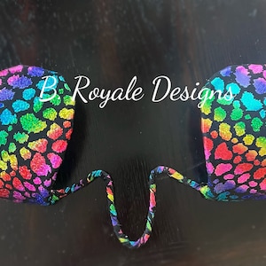 Könnte beinhalten: Ein Paar Regenbogen-Leoparden-Pasties mit schwarzen Trägern. Die Pasties sind aus einem weichen, dehnbaren Stoff gefertigt und perfekt, um jedem Outfit einen Hauch von Glamour zu verleihen.