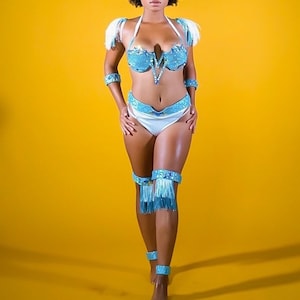 May include: A woman wearing a blue and white costume with fringe details. She is standing on a yellow background and has her hair pulled back.