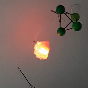 May include: Three hanging light fixtures, one is a white cloud-shaped light with a warm orange glow, another is a geometric, rainbow-colored, diamond-shaped light, and the last is a green geometric mobile with four spheres.