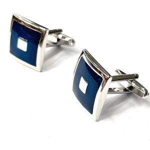 Puede incluir: Un par de gemelos de plata con un diseño cuadrado de esmalte azul. El centro de cada cuadrado tiene un cuadrado blanco más pequeño.