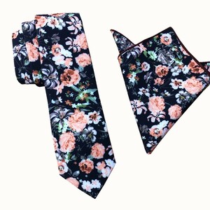 May include: A black tie and pocket square set with a floral pattern featuring peach and white flowers on a black background.