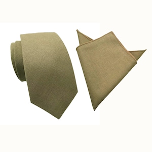 Puede incluir: Un conjunto de corbata y pañuelo de bolsillo de color verde. La corbata está hecha de un tejido texturizado y tiene una punta puntiaguda. El pañuelo de bolsillo es de un solo color y tiene una forma ligeramente redondeada.