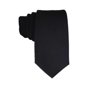 May include: A plain black tie, folded and presented on a white backdrop. The tie has a slim design and a textured surface. This formal accessory is suitable for various occasions.