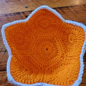 May include: A crocheted star-shaped bowl with an orange interior and a white border.