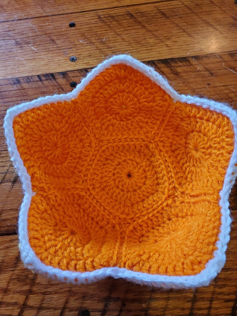 May include: A crocheted star-shaped bowl with an orange interior and a white border.