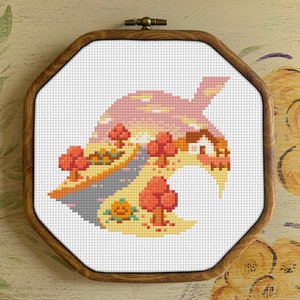 May include: Cross-stitch embroidery of a fall-themed landscape with a house, trees, and a road, all within the shape of a green leaf.
