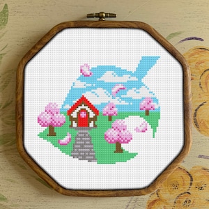May include: Cross-stitch embroidery depicting a red house with a white door and a green roof, surrounded by pink cherry blossom trees on a green lawn. The house is situated on a blue leaf with white clouds and a blue sky.
