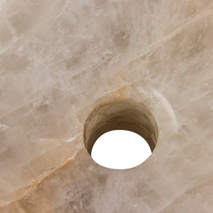 Może przedstawiać: Zbliżenie na okrągły, biały, naturalny kamień z otworem w środku. Kamień ma szorstką, fakturowaną powierzchnię.