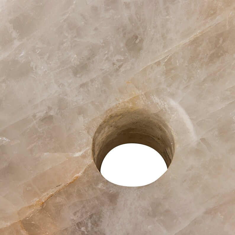 Może przedstawiać: Zbliżenie na okrągły, biały, naturalny kamień z otworem w środku. Kamień ma szorstką, fakturowaną powierzchnię.