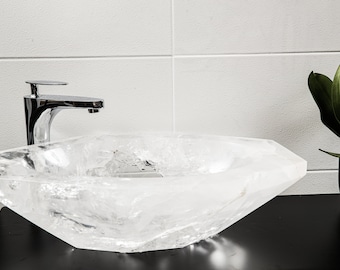 May include: A clear crystal sink with a chrome faucet. The sink is on a black countertop.