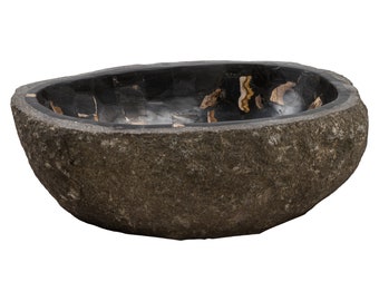 May include: A natural stone vessel sink with a rough, textured exterior. The interior features a mosaic of black and brown polished stone. The sink has an oval shape and is designed for bathroom use.