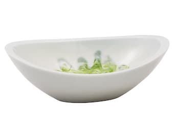 Puede incluir: Un bol ovalado de cerámica blanca con un diseño marmoleado verde y blanco. El bol es poco profundo y tiene un acabado liso y brillante.