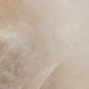 Może przedstawiać: Zbliżenie gładkiego, białego, naturalnego kamienia o lekko prześwitującym wyglądzie. Kamień ma subtelny, jasnobrązowy odcień i fakturowaną powierzchnię.