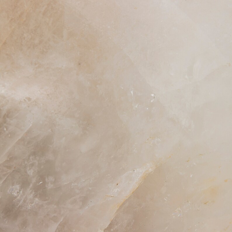 Może przedstawiać: Zbliżenie gładkiego, białego, naturalnego kamienia o lekko prześwitującym wyglądzie. Kamień ma subtelny, jasnobrązowy odcień i fakturowaną powierzchnię.