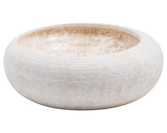May include: A round, low-profile bowl with a thick, textured exterior featuring horizontal grooves in a light off-white finish. The interior of the bowl has a smooth, polished surface with a marbled beige and cream pattern throughout the basin.