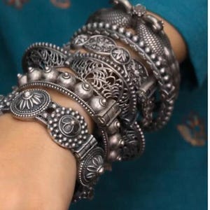 May include: A stack of silver bracelets with intricate designs, including floral patterns and beaded accents.
