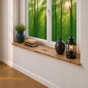 May include: A rustic wooden windowsill displays a small potted plant in a blue vase, two books, a textured black vase, and a black lantern with a lit bulb. The window overlooks a green forest scene.