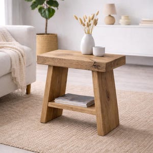 Op de afbeelding: Een kleine, rechthoekige houten bijzettafel met een onderste plank. De tafel is gemaakt van lichtbruin hout en heeft een natuurlijke, rustieke uitstraling. Een witte vaas met gedroogde bloemen en een klein wit kopje staan erop. De tafel is 61 cm lang, 41 cm breed en 46 cm hoog.